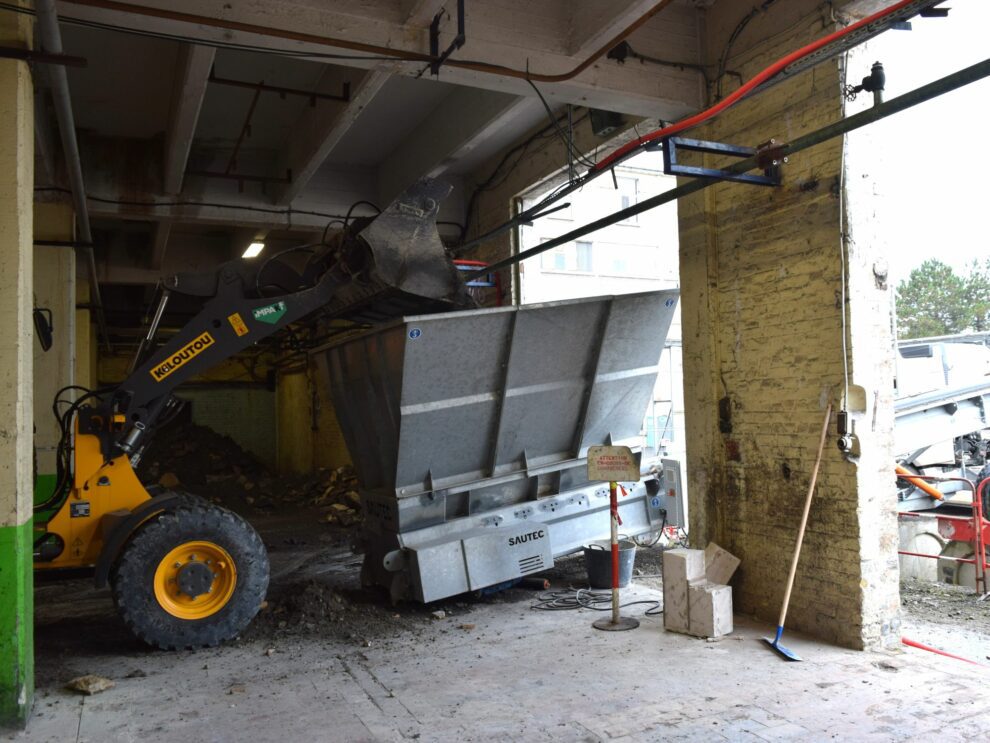 Een lader stort materiaal in de trechter van een bouwband.