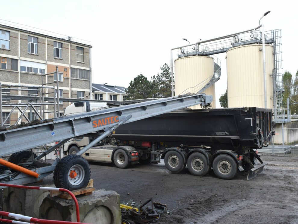 Een transportband stort puin in een container.